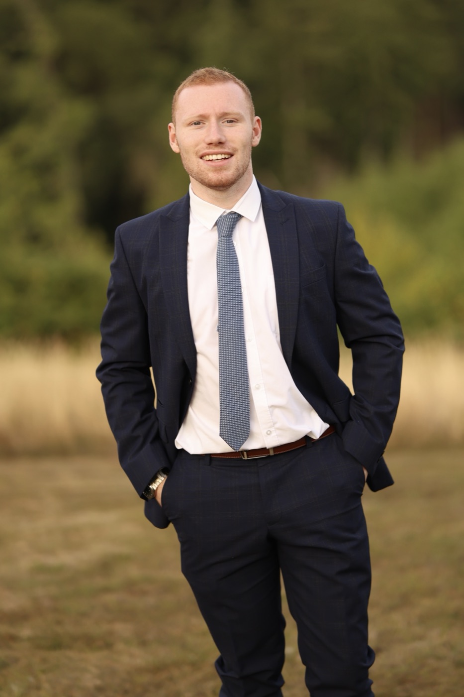Joseph Carey in a navy suit, standing in a field