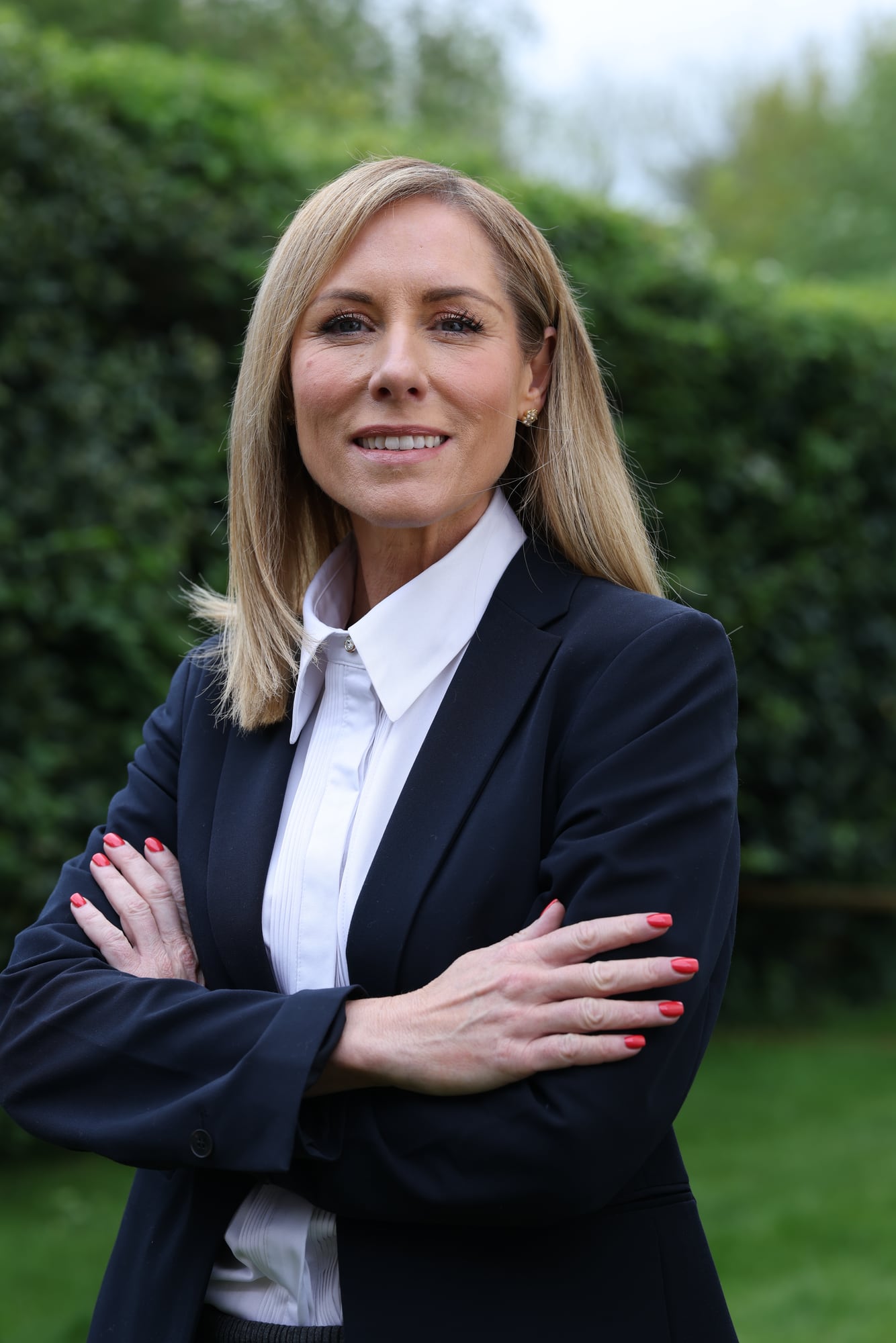 A business portrait: arms crossed, a hedge behind